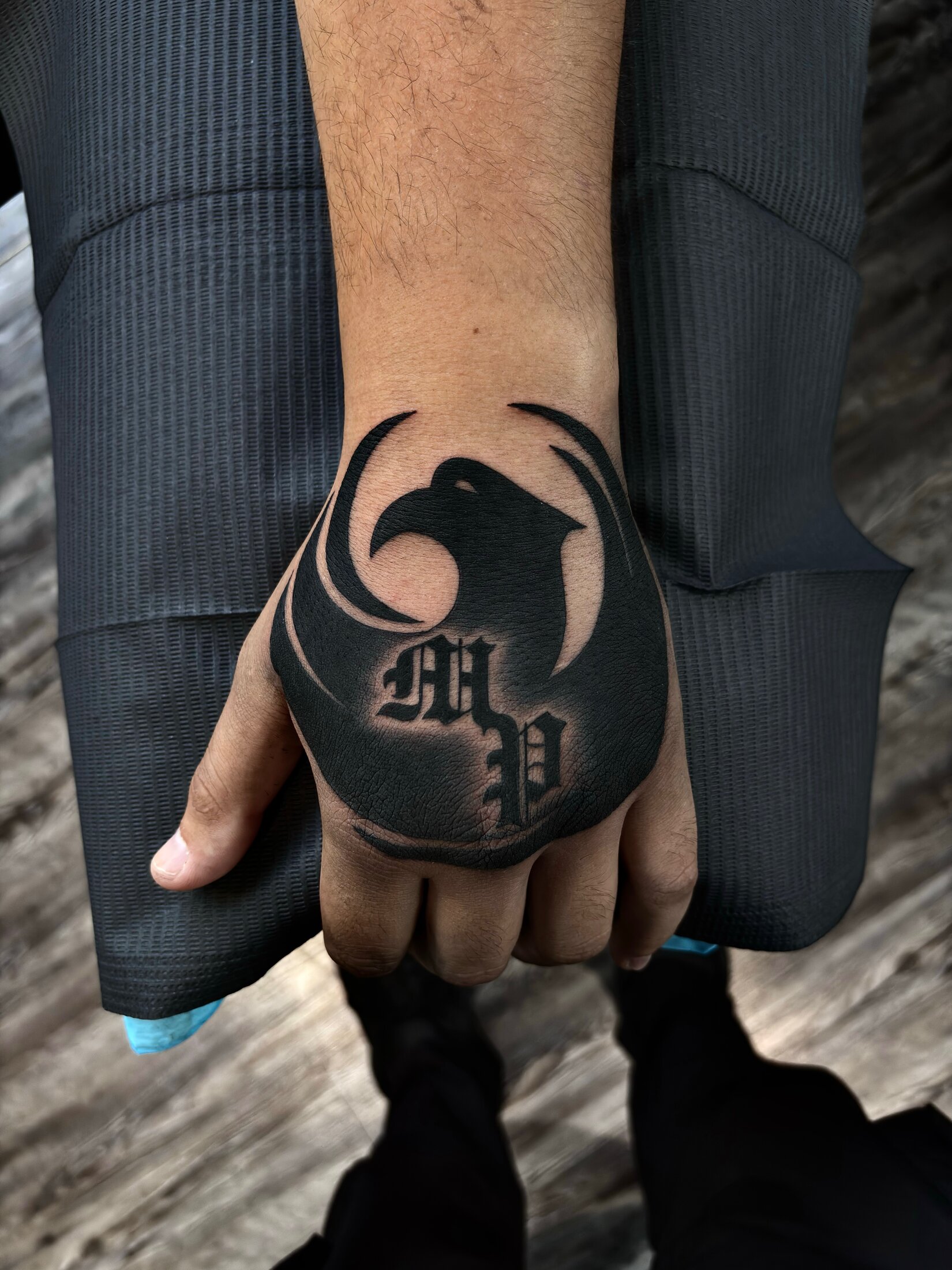 Black and grey eagle and blackletter initials tattoo covering an older piece on a hand