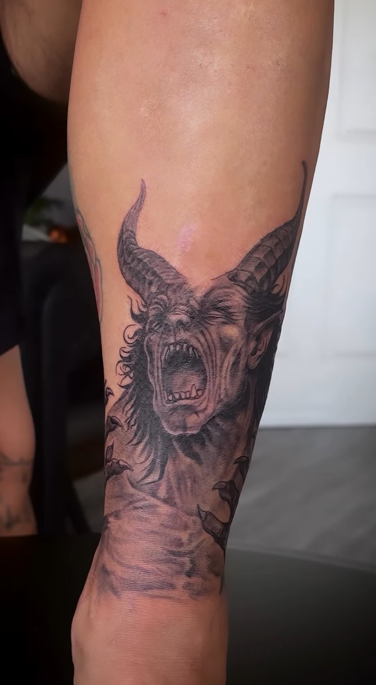 Black and grey realism tattoo of a screaming horned goat demon on a forearm