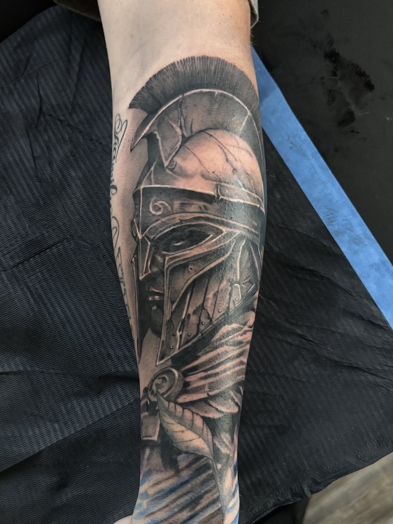 Black and grey realism tattoo of a Spartan helmet on a forearm