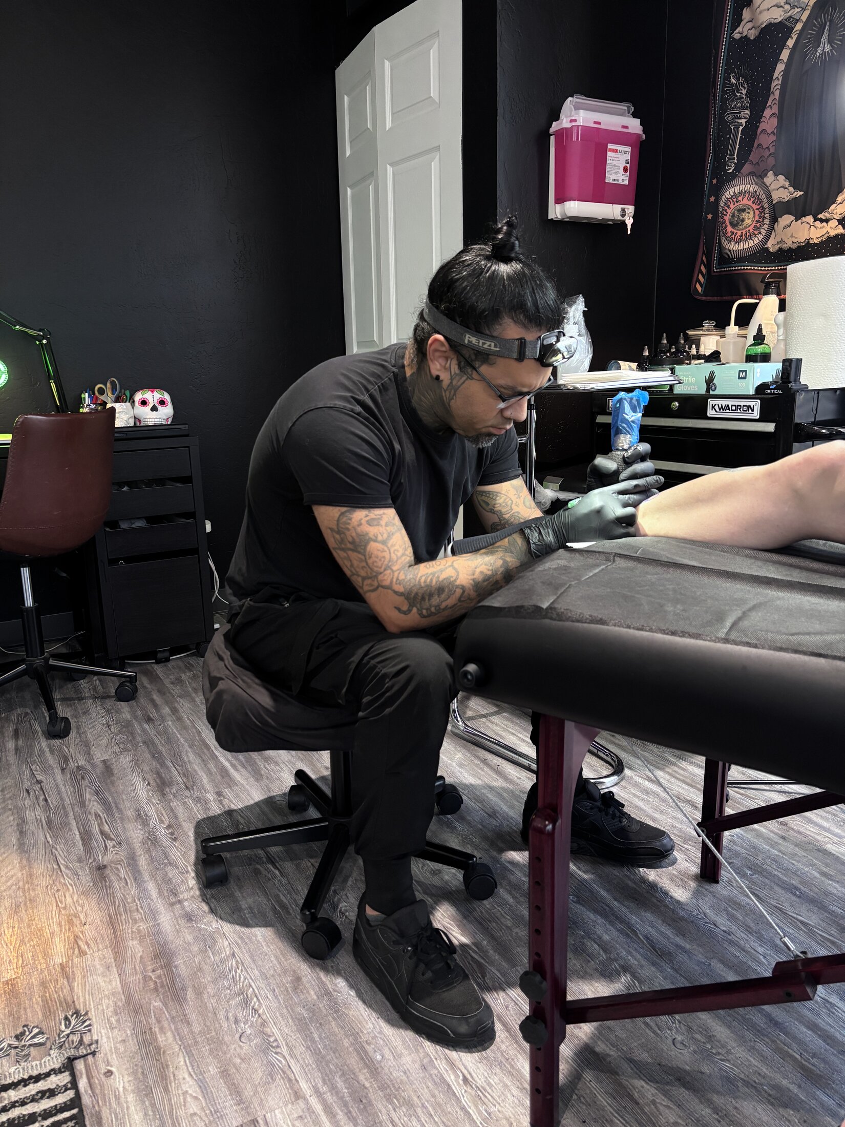 Gloved hand holding a tattoo machine over skin in dramatic single light